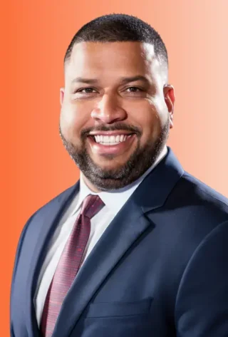 Joe Susaña, smiling founder of Lightning Leads Pro, wearing a suit and tie against an orange background, representing a veteran-owned digital marketing agency for home service businesses.